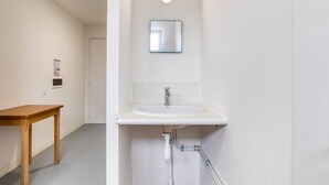 Ein Badezimmer mit einem weißen Waschbecken, einem Spiegel darüber und einem Holztisch im angrenzenden Raum.