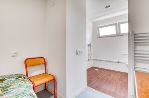 A small, single-room apartment with a bed, a chair, a shower area, and a window. - Room with Shared Terrace and Wi-Fi, 10 Minutes from the Beach (Mudaison)