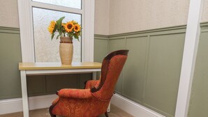 Ein Stuhl mit gemustertem Stoff, ein Holztisch und eine Vase mit Sonnenblumen auf einem Fensterbrett.