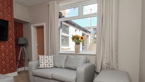 A living room with a grey sofa, a matching ottoman, a floor lamp, and a window with curtains.