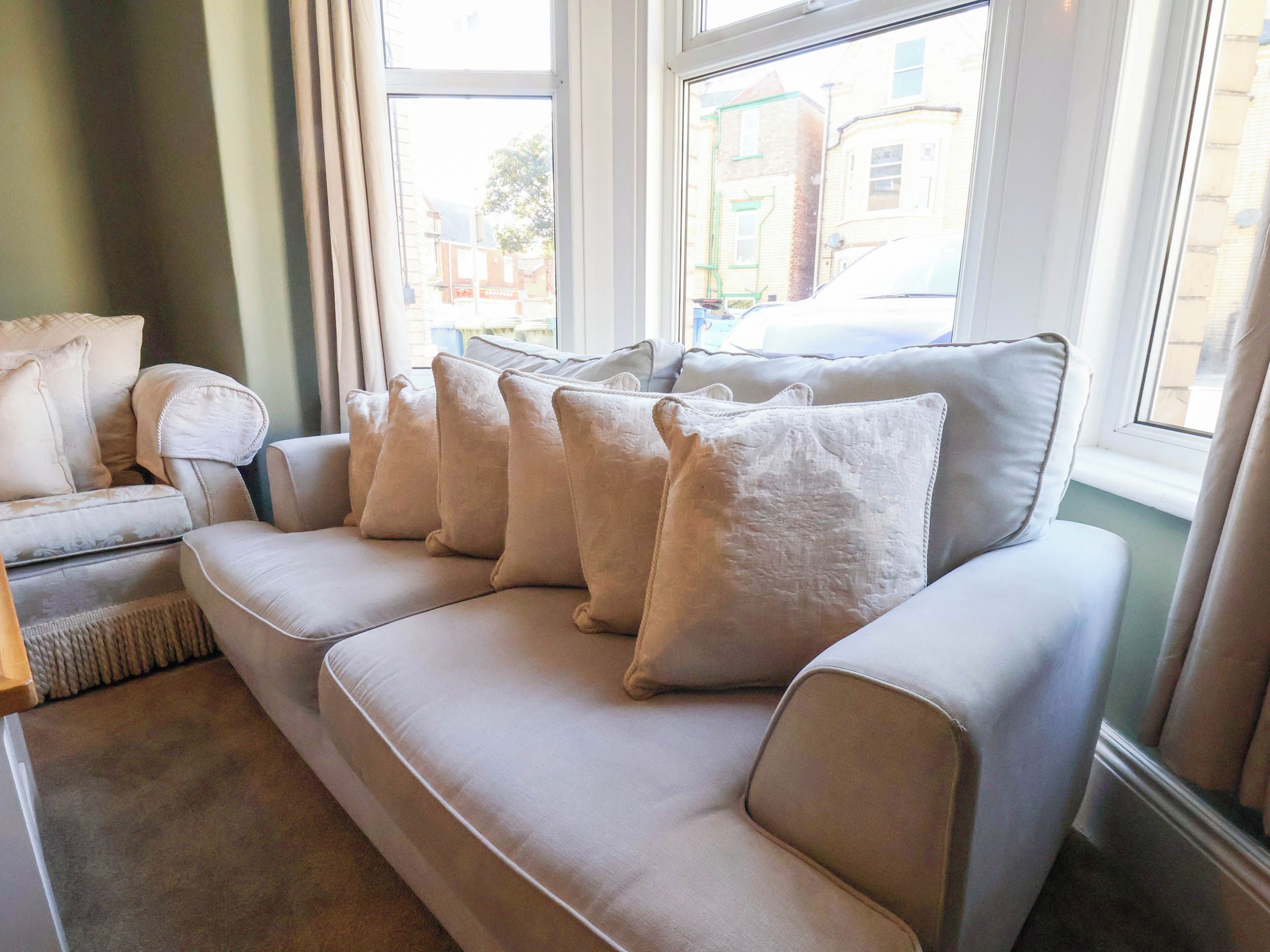 Ein beiges Sofa mit vielen Kissen, platziert in der Nähe eines Fensters mit Blick auf Gebäude.