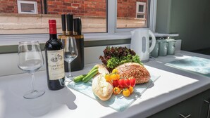 A table with a bottle of wine, a glass, a loaf of bread, vegetables, and a kettle.