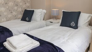 Ein Hotelzimmer mit zwei Betten, einem Nachttisch mit Lampe, einem Bild an der Wand und einem floralen Wandmuster.