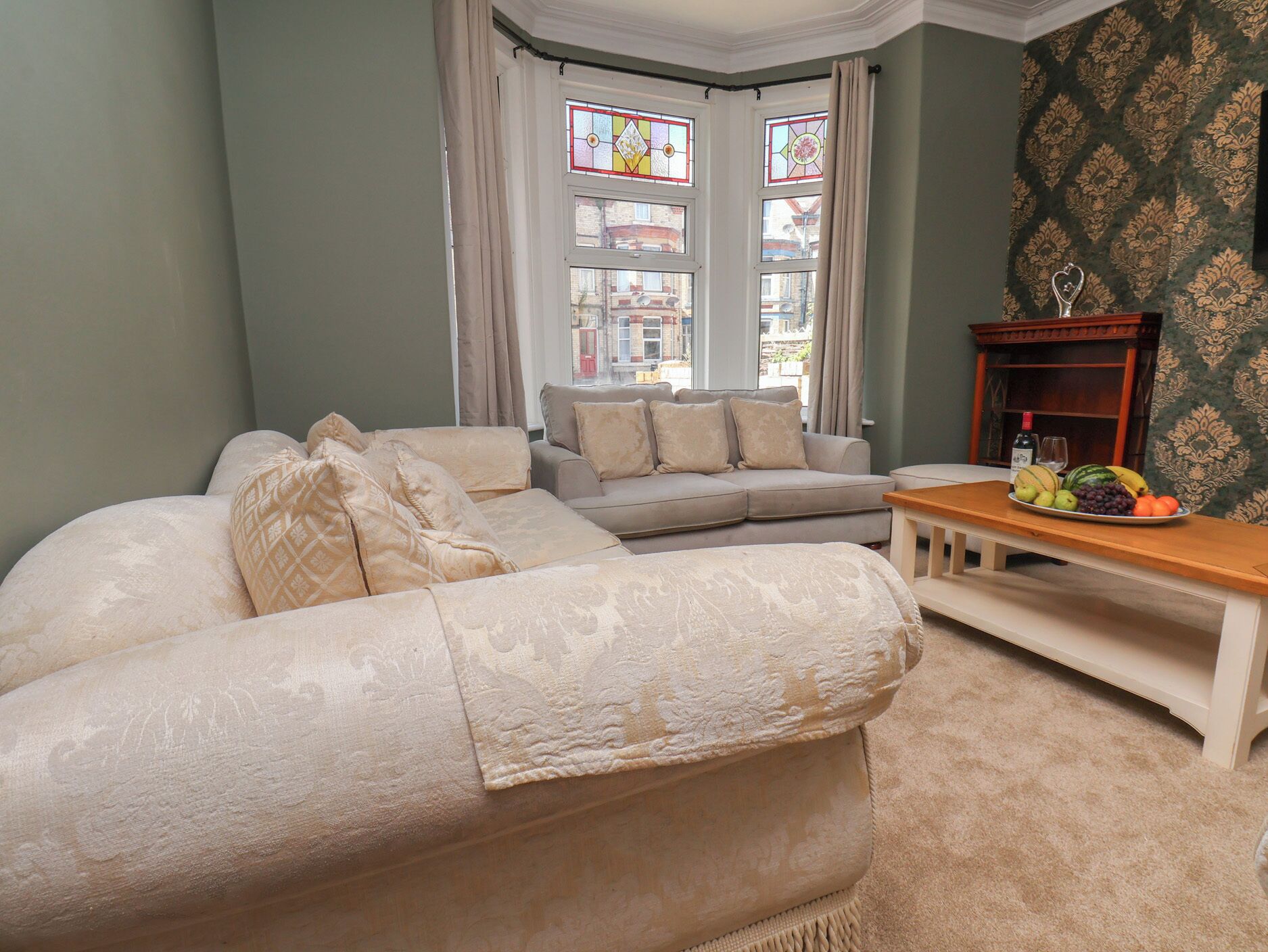 A living room with a sofa, a coffee table with fruit, and a view through a bay window.