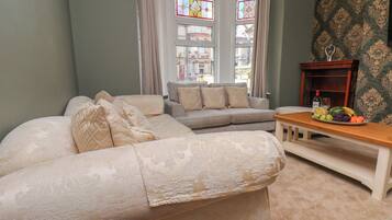 A living room with a sofa, a coffee table with fruit, and a view through a bay window.