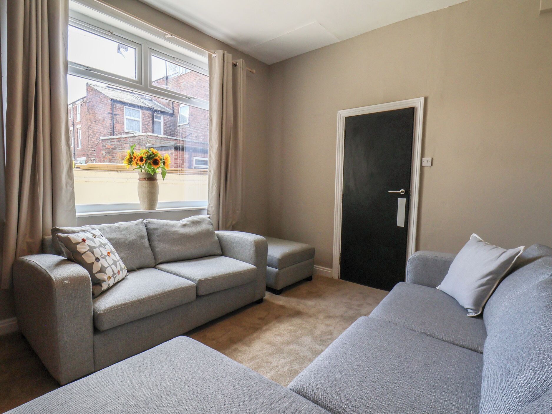 A living room with a grey sofa, a small table with a vase of flowers, and a door.