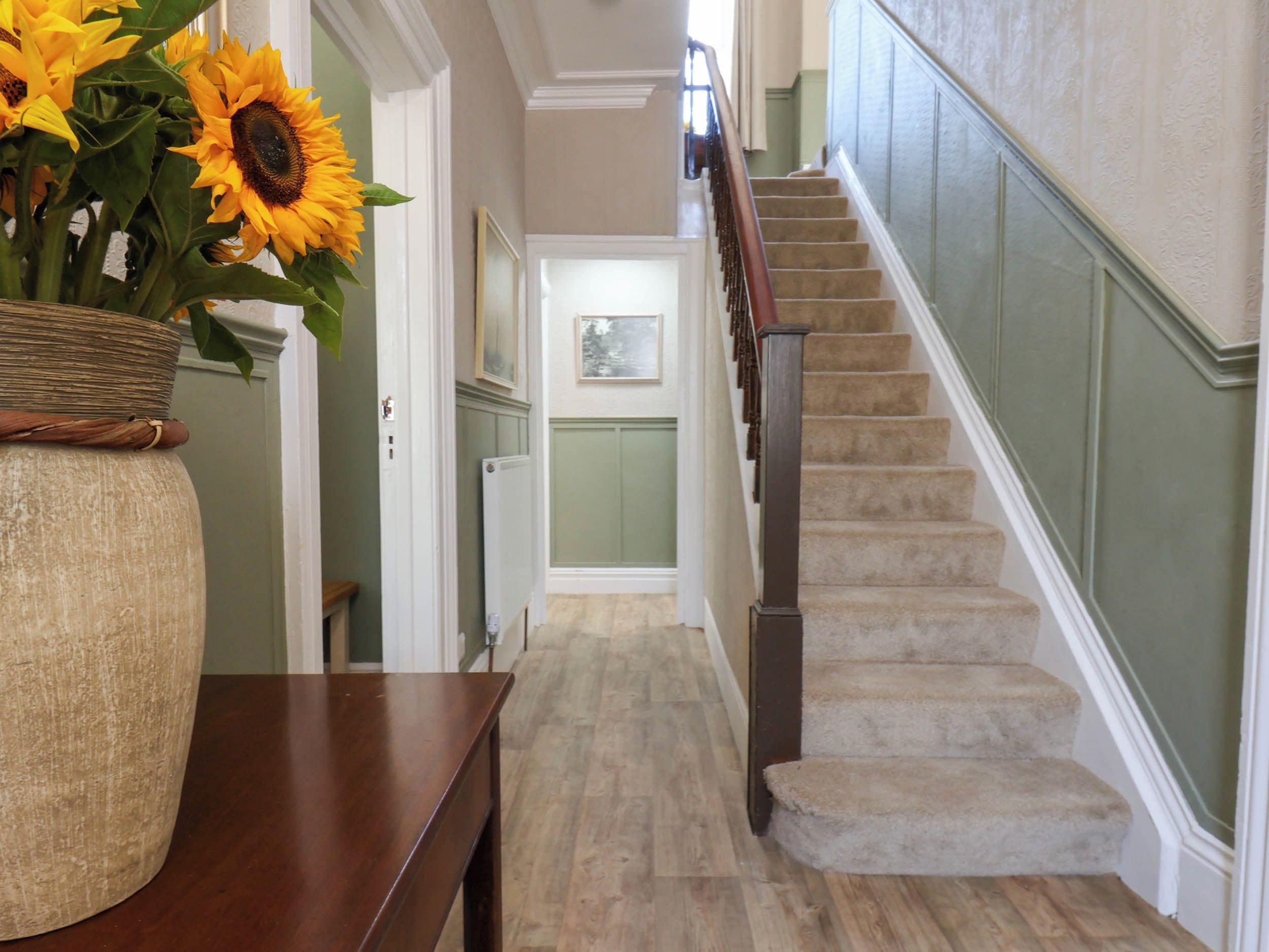 A hallway with a wooden bench, a vase of sunflowers, and a staircase with a wooden handrail.
