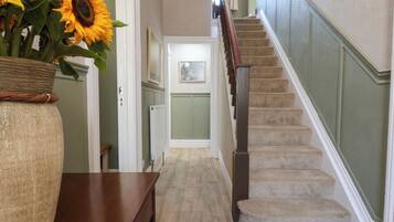 A hallway with a wooden bench, a vase of sunflowers, and a staircase with a wooden handrail.
