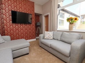 A living room with a grey sofa, a matching armchair, a flat-screen TV mounted on the wall, and a window with a view of the outside. - Lansdowne Grange (Bridlington)