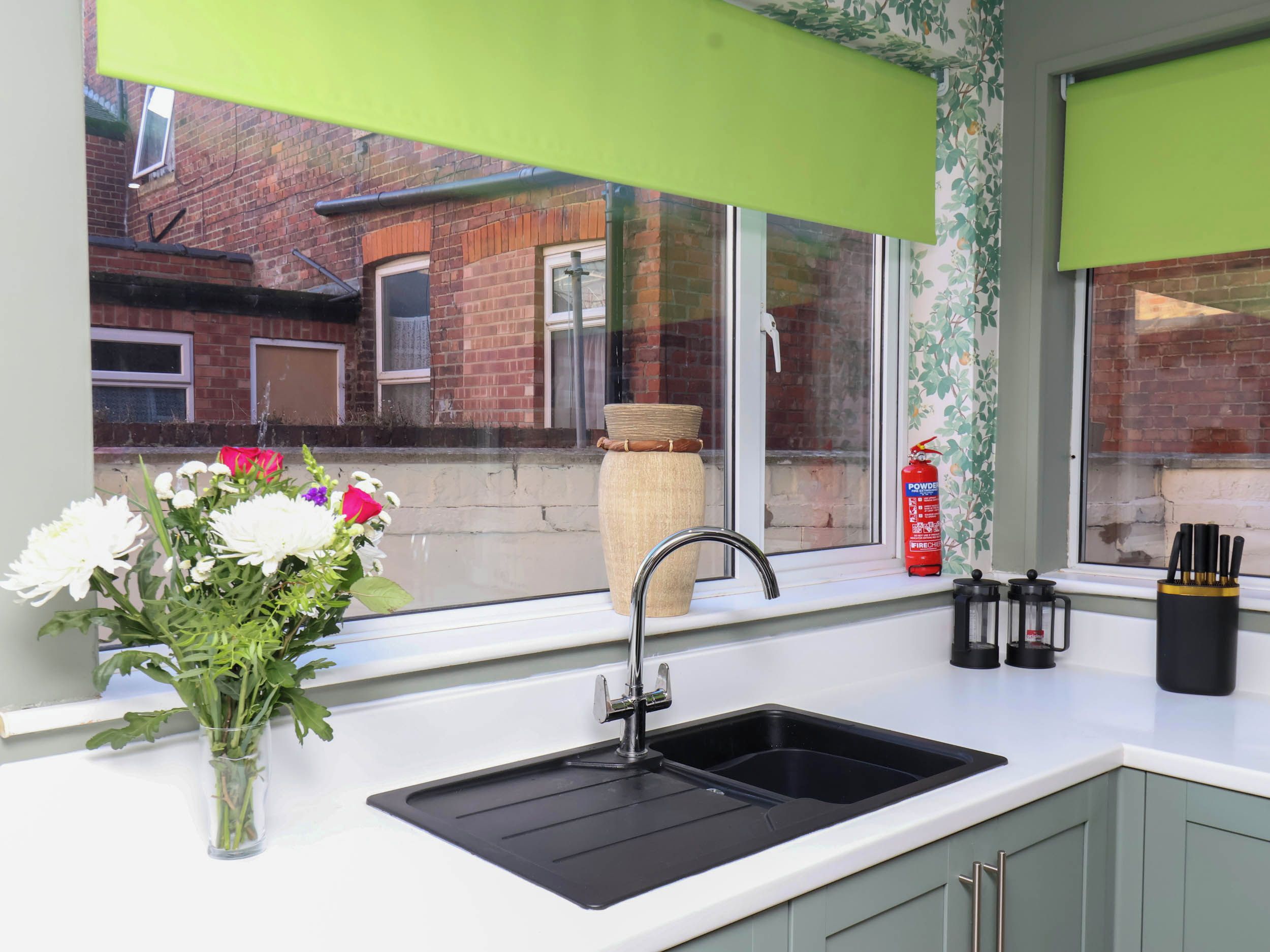 A kitchen with a sink, a window with a view of a brick building, and a vase with flowers on the windowsill.