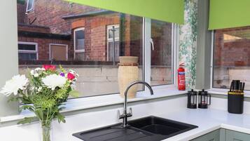 A kitchen with a sink, a window with a view of a brick building, and a vase with flowers on the windowsill.