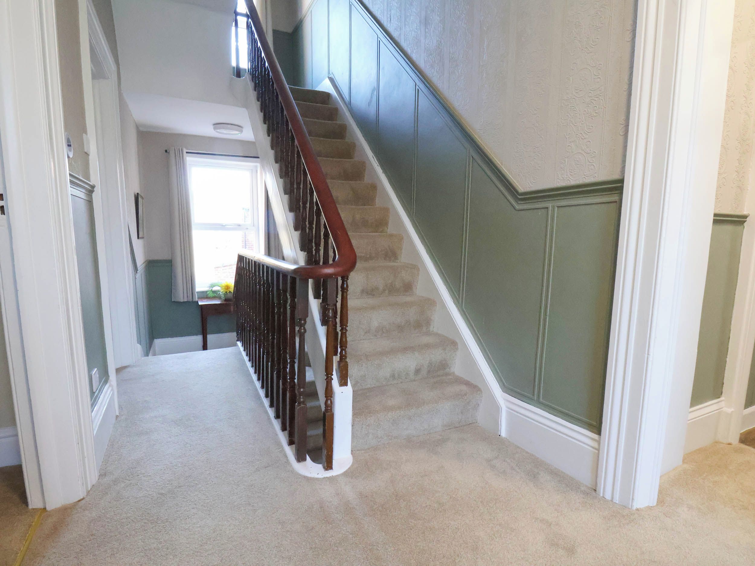 A carpeted staircase with a wooden handrail and a green wall.