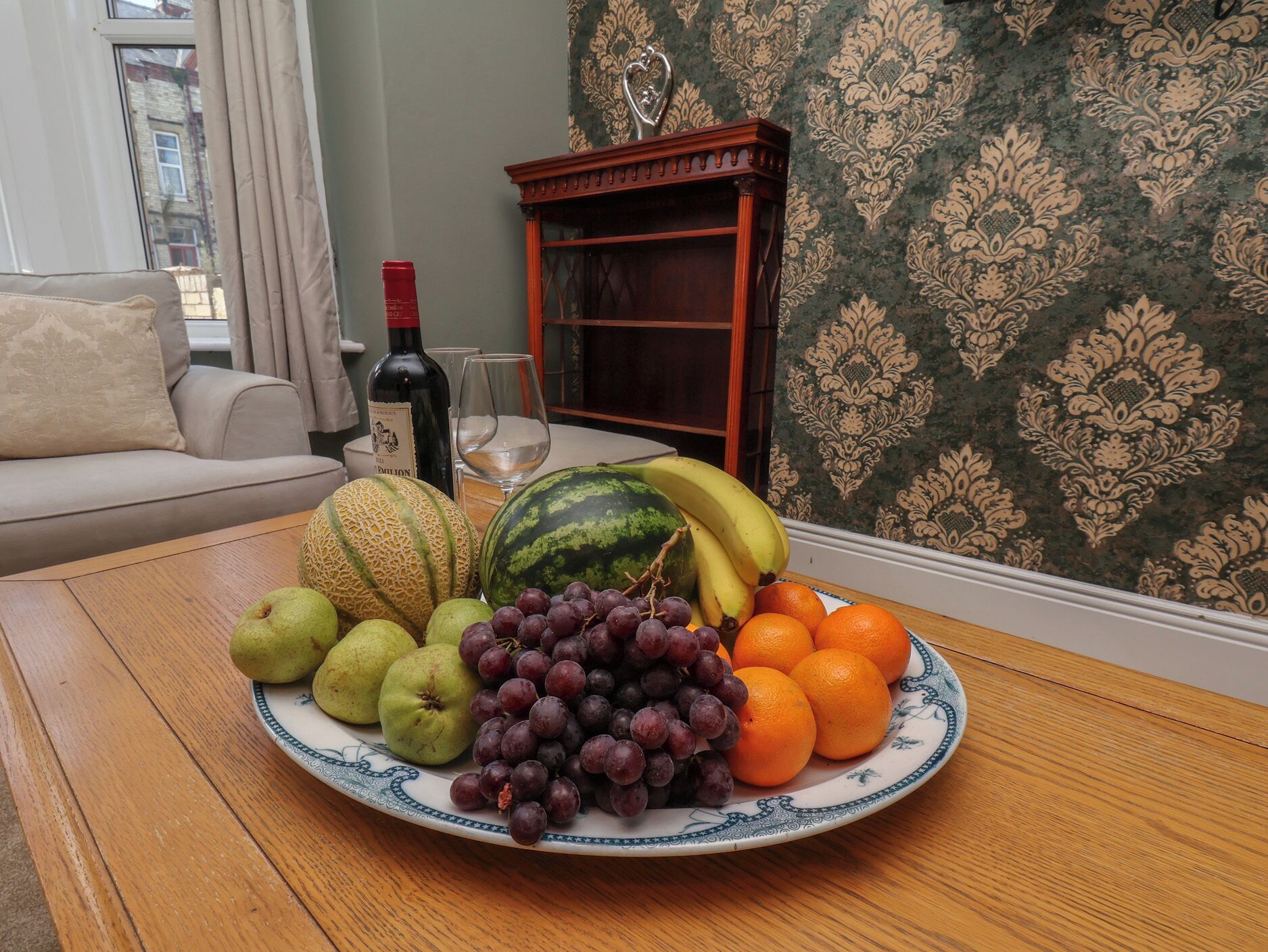 Una mesa de comedor con un plato de fruta, una botella de vino y una copa.