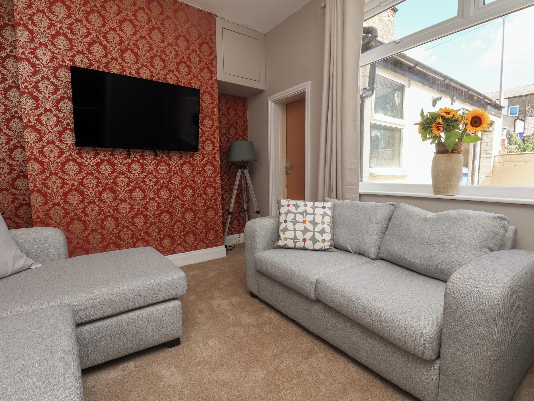 Salón con sofá gris, un sillón a juego, televisor de pantalla plana montado en la pared, una lámpara de trípode y ventana con vistas al exterior.