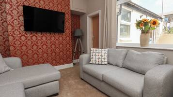 Salón con sofá gris, un sillón a juego, televisor de pantalla plana montado en la pared, una lámpara de trípode y ventana con vistas al exterior.