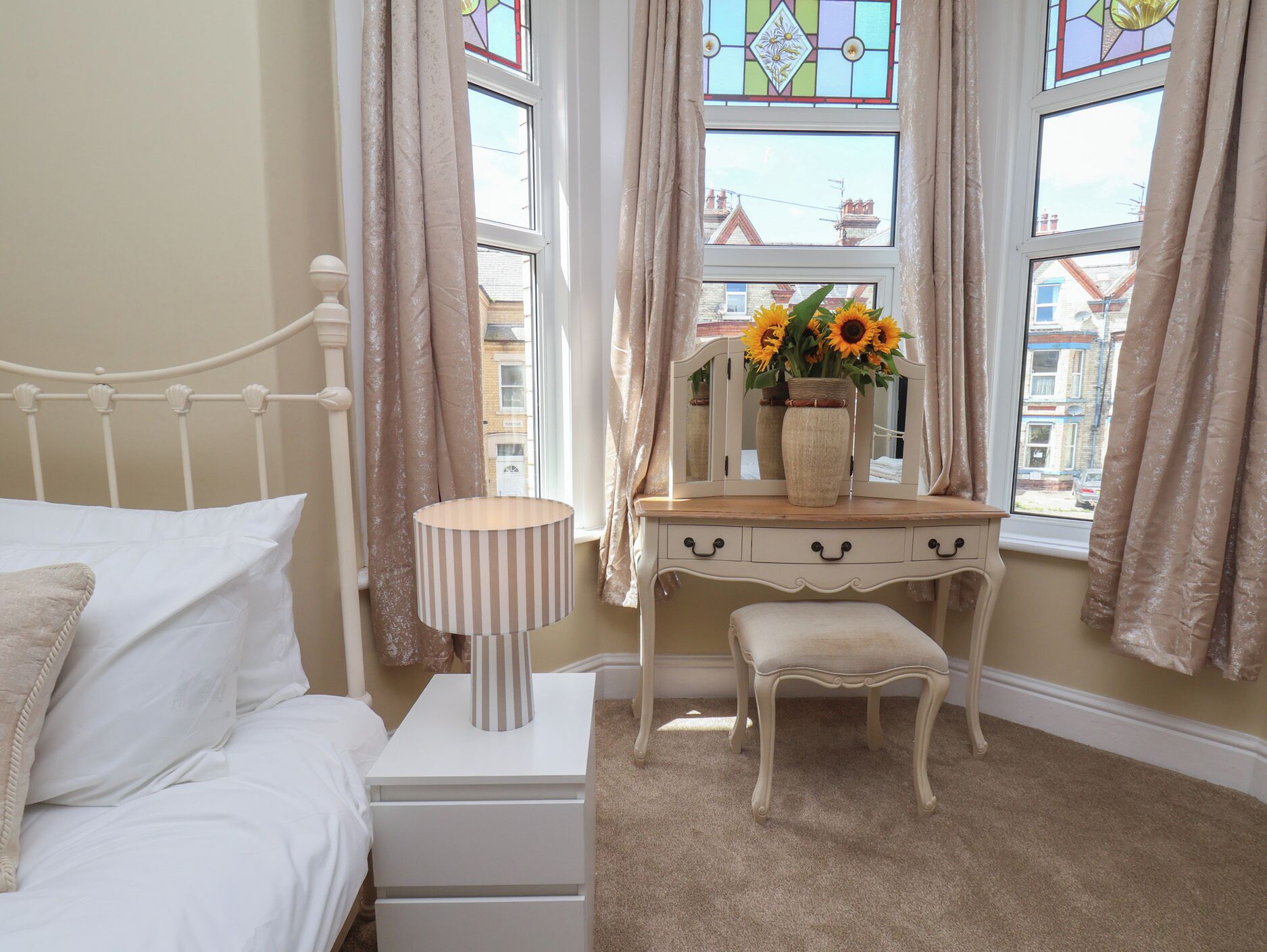 A bedroom with a bed, a bedside lamp, a dresser with a mirror, and a window with curtains.