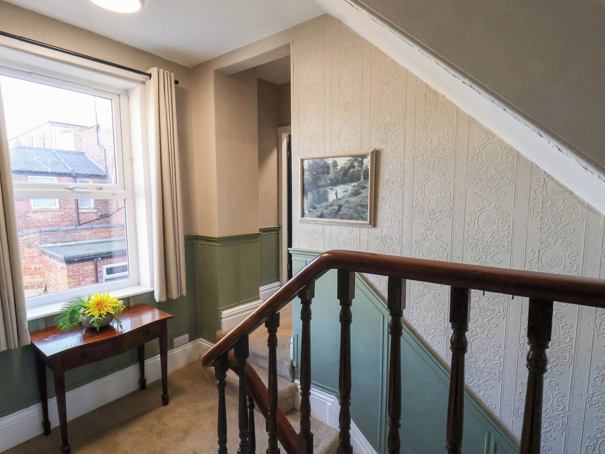 A staircase with a wooden handrail, a window with curtains, and a wall with patterned wallpaper.