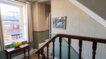 A staircase with a wooden handrail, a window with curtains, and a wall with patterned wallpaper.