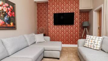 A living room with a sectional sofa, a flat-screen TV mounted on the wall, and patterned wallpaper.