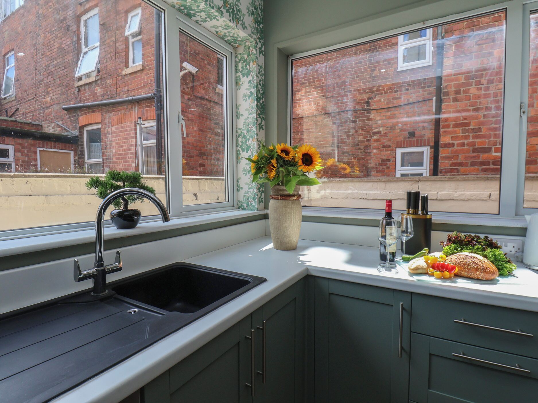 A kitchen with a sink, a vase with sunflowers, and a window with a view of brick buildings.