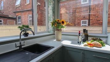Una cocina con un lavabo, un florero con girasoles y una ventana con vistas a edificios de ladrillo.