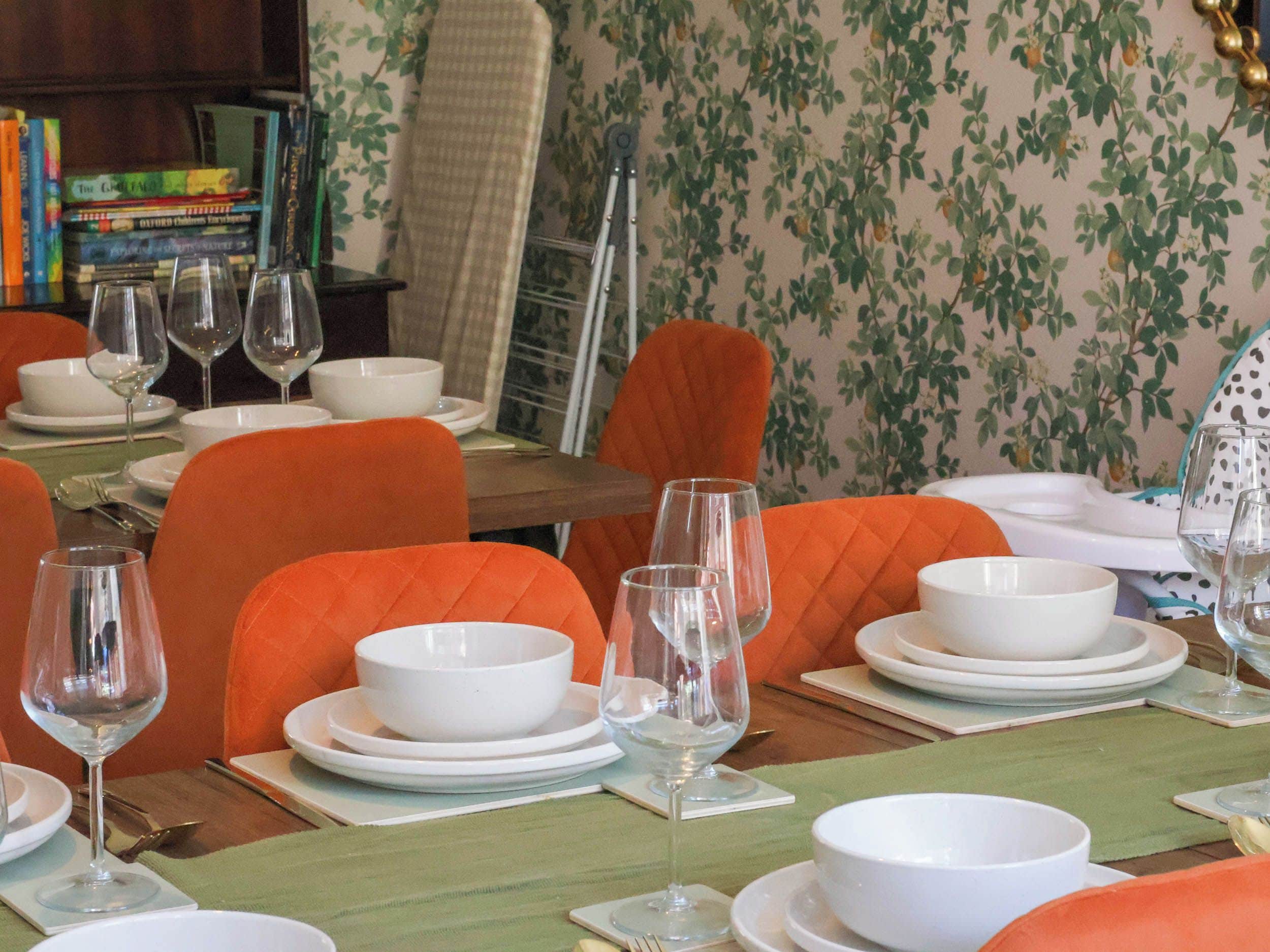 Un comedor con sillas naranjas, platos blancos y copas de vino dispuestas para una comida.
