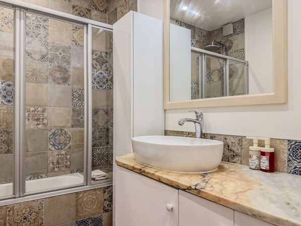 A bathroom with a white sink, a mirror, and a shower with patterned tiles. - #409 Central Albufeira Getaway with Shared Pool (Albufeira)