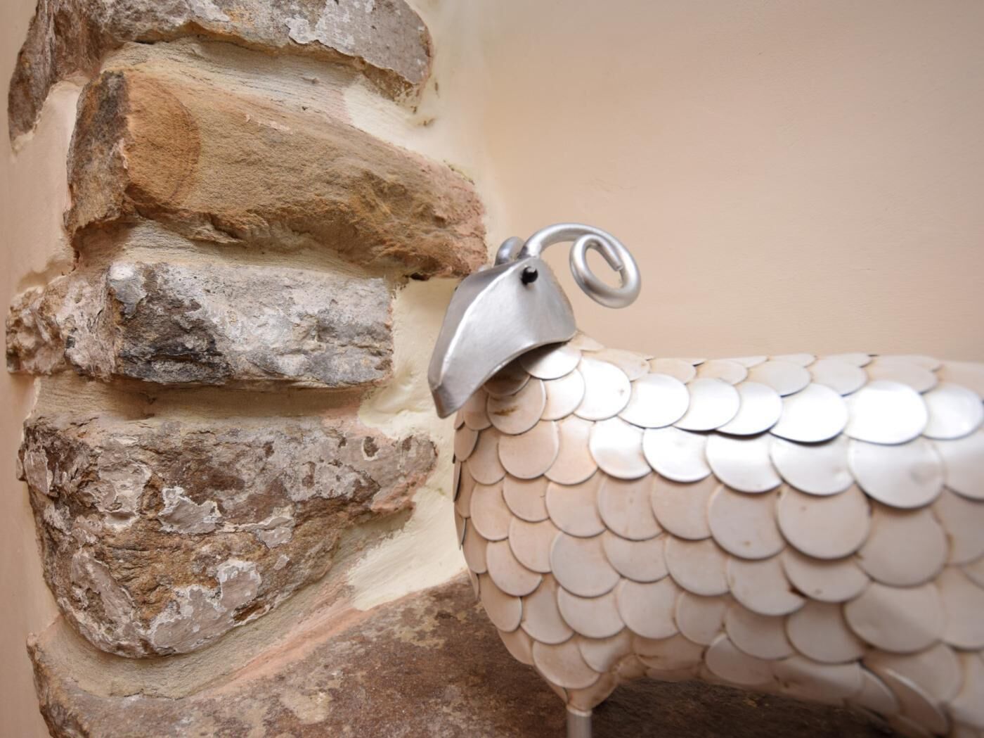 Een decoratief metalen schaap voor een ruwe stenen muur.