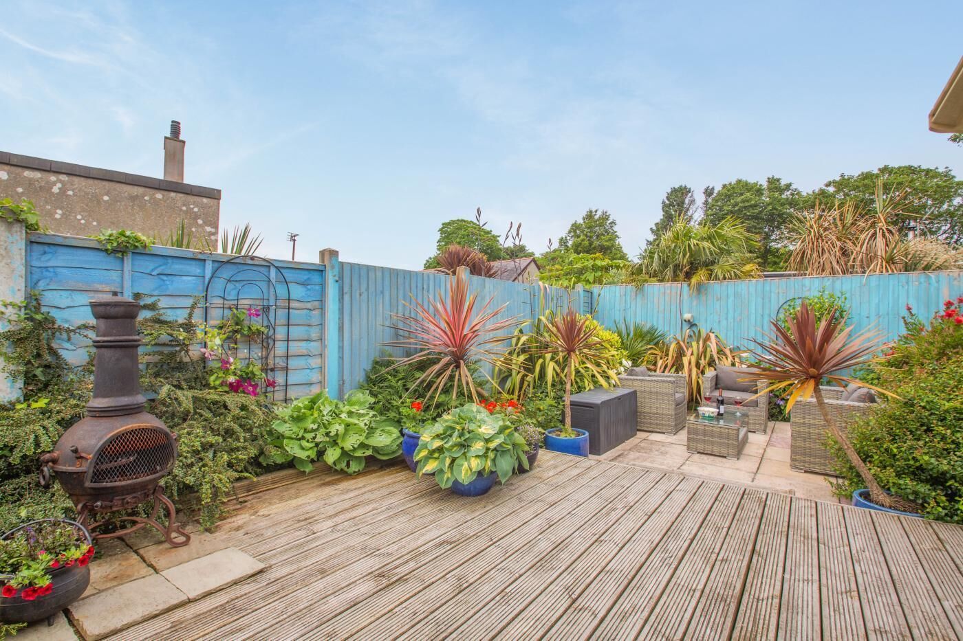 Una terraza de madera con plantas en macetas, una estufa de metal y mobiliario exterior.