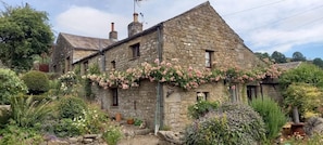 A stone building with a garden in front, featuring a variety of plants and flowers. - 1 Bed in Richmond (oc-44401) (Healaugh)