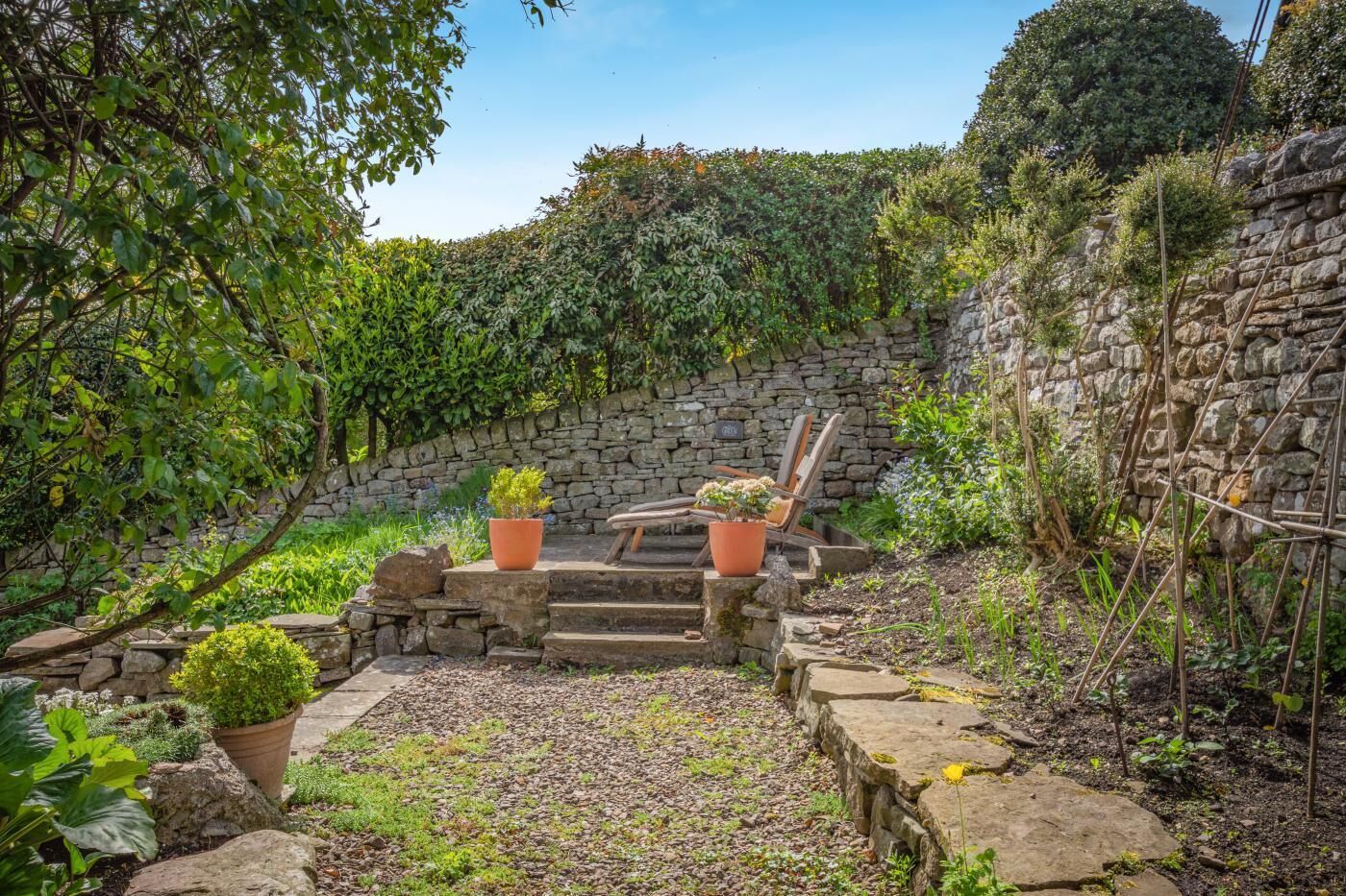 Un muro de piedra, un banco de madera y plantas en macetas en un jardín.