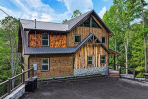 A two-story wooden cabin with a stone foundation, large windows, and a metal roof. - Forest Views, Hot Tub, Fireside Nights, Theater room & Family Fun (Sevierville)
