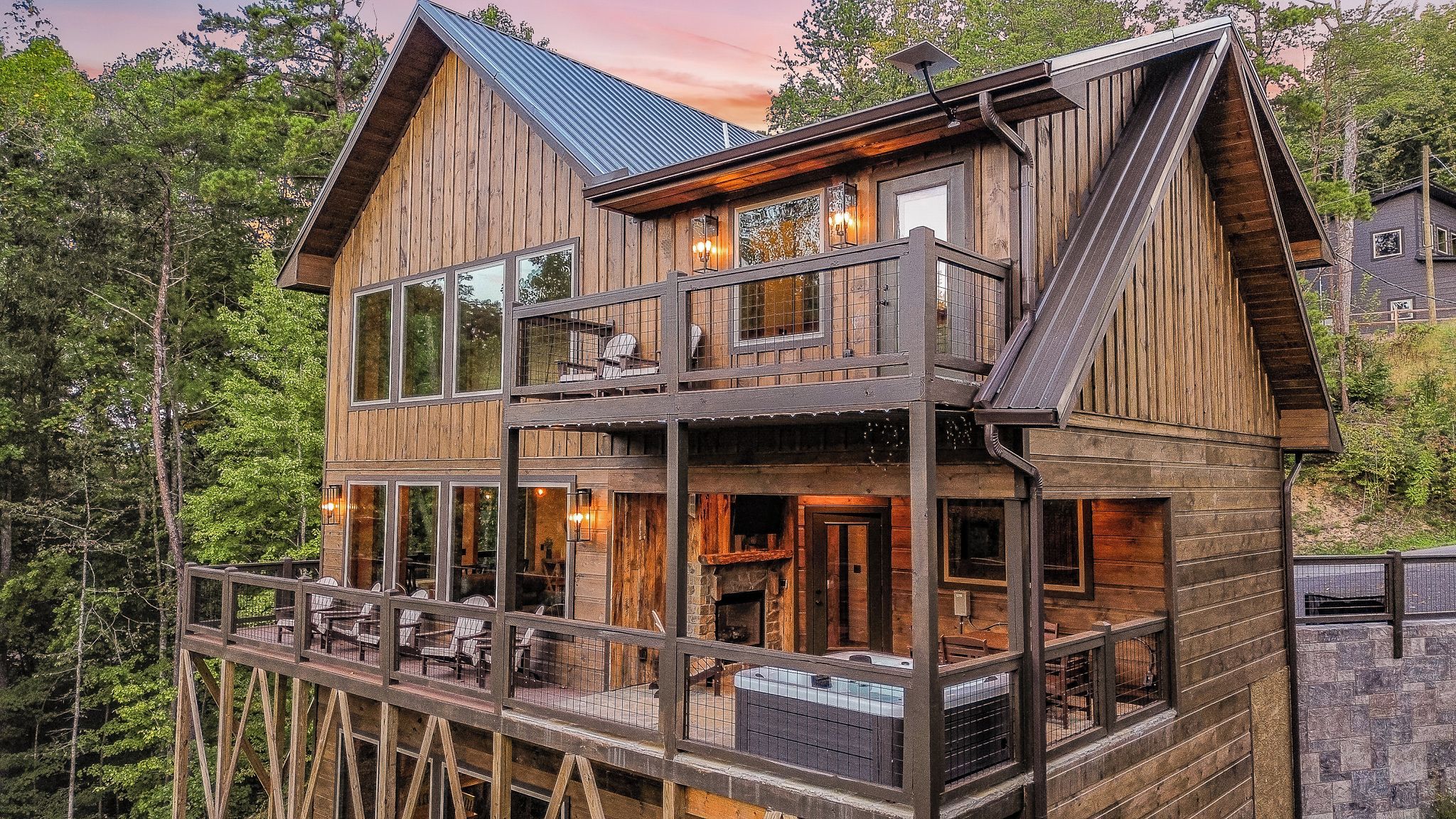 A two-story wooden cabin with a balcony, large windows, and a stone foundation.