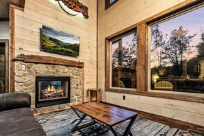 A cozy interior with a stone fireplace, a large window with a view of trees, and a leather couch. - Forest Views, Hot Tub, Fireside Nights, Theater room & Family Fun (Sevierville)
