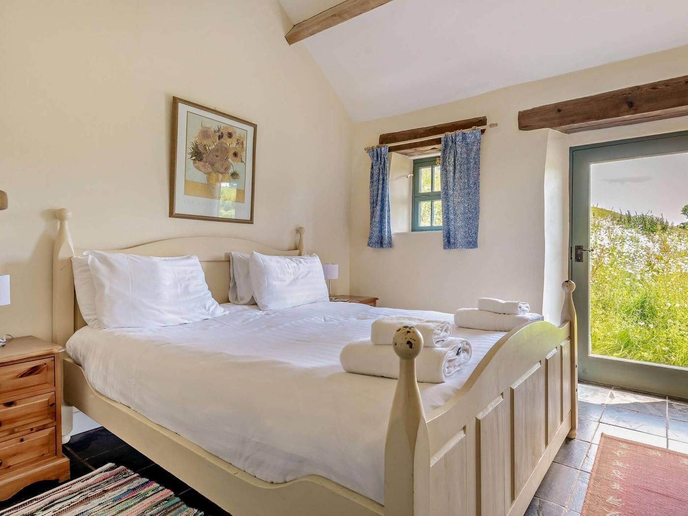 A bedroom with a bed, a nightstand, a window with curtains, and a view of greenery outside.