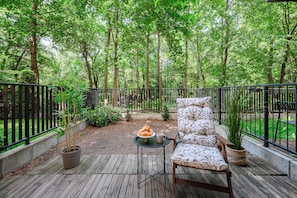 A wooden deck with a chair and table, surrounded by a metal fence, overlooking a lush green forest. - Lumina 2BR Apart with Two Patio  (Warszawa)
