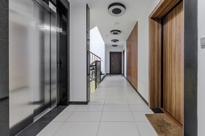 A modern hallway with a metallic elevator, wooden doors, and a tiled floor. - Lumina 2BR Apart with Two Patio  (Warszawa)
