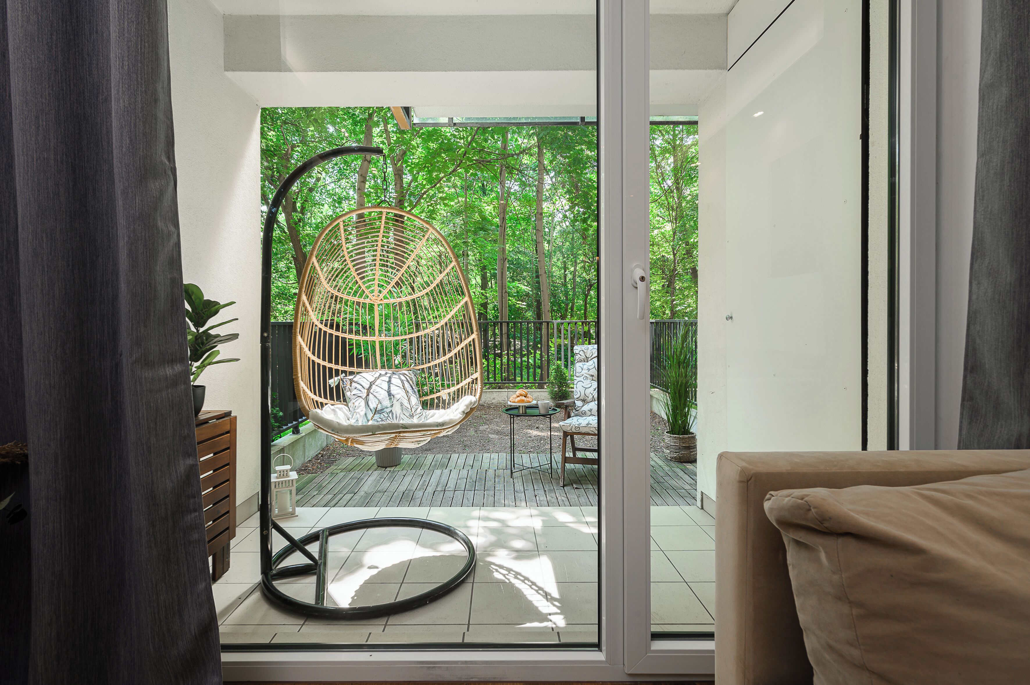 Une pièce dotée d’une porte vitrée donnant sur un espace extérieur aménagé avec un fauteuil suspendu, une petite table et un pot de fleurs.