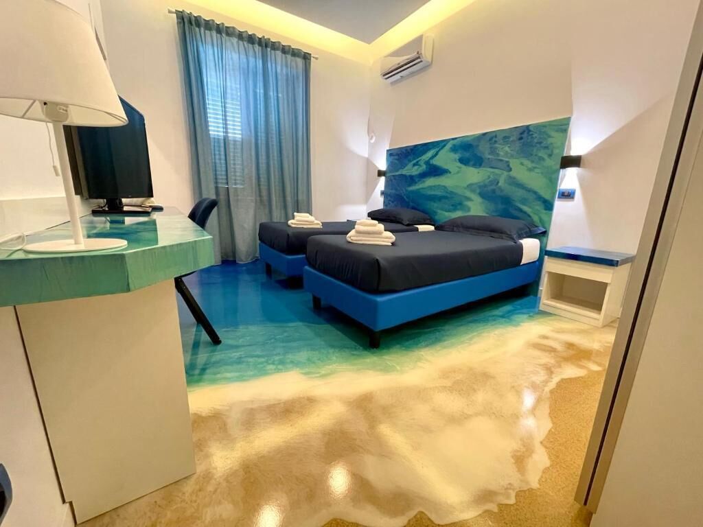 Ein Hotelzimmer mit einem Bett, einem Schreibtisch, einem Sessel, einem Fernseher und einem großen, abstrakten Wandbild.