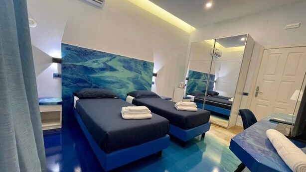 Una habitación de hotel moderna con dos camas, un espejo grande y suelo azul.