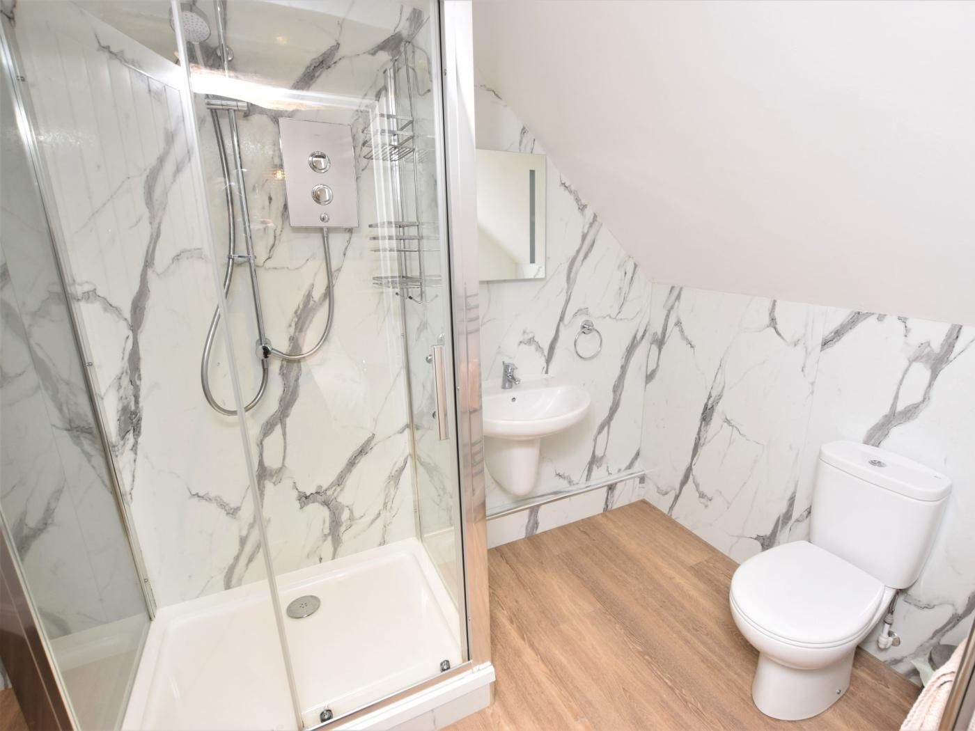 Een badkamer met een douchecabine van glas, een witte wastafel, een toilet en muren met een marmerlook.