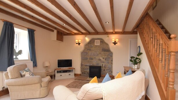 A cozy living room with a stone fireplace, wooden beams, a television, and a staircase. - 2 Bed in Ashford In The Water (oc-pk502) (Ashford in the Water)