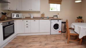 A kitchen with white cabinets, a microwave, a washing machine, and a dining area with a table and chairs. - 2 Bed in Ashford In The Water (oc-pk502) (Ashford in the Water)