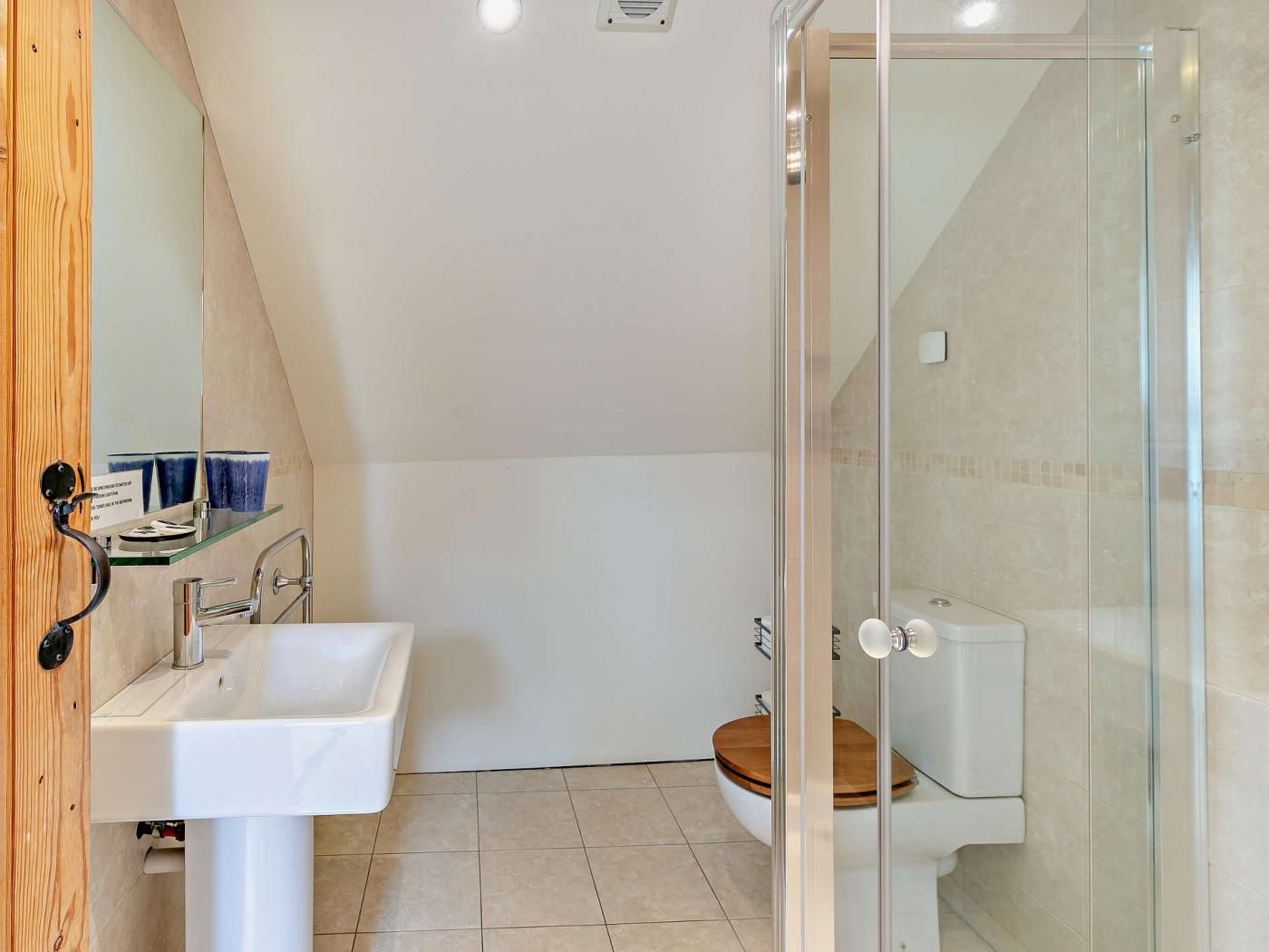 A modern bathroom with a glass shower enclosure, a white sink, and a wooden toilet.