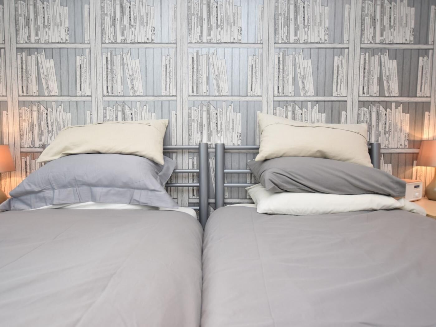 Una cama doble con cabecera, dos mesitas de noche y una pared con estantería.