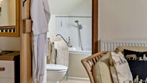 Ein Badezimmer mit Toilette, Dusche und einem Holzstuhl mit Kissen.