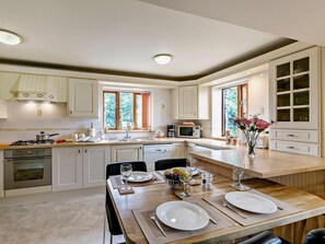 Eine moderne Küche mit weißen Schränken, ein Essbereich mit einem Holztisch, gedeckt für zwei Personen, und Blick ins Grüne.