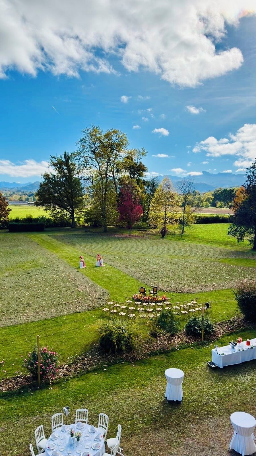Een bruiloftlocatie buiten, met een gazon, witte stoelen en ronde tafels klaar voor een receptie.