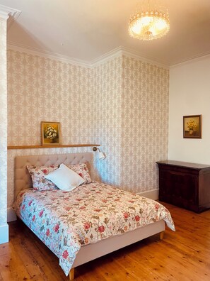 Un dormitorio con cama, mesita de noche, candelabro y papel tapiz estampado.