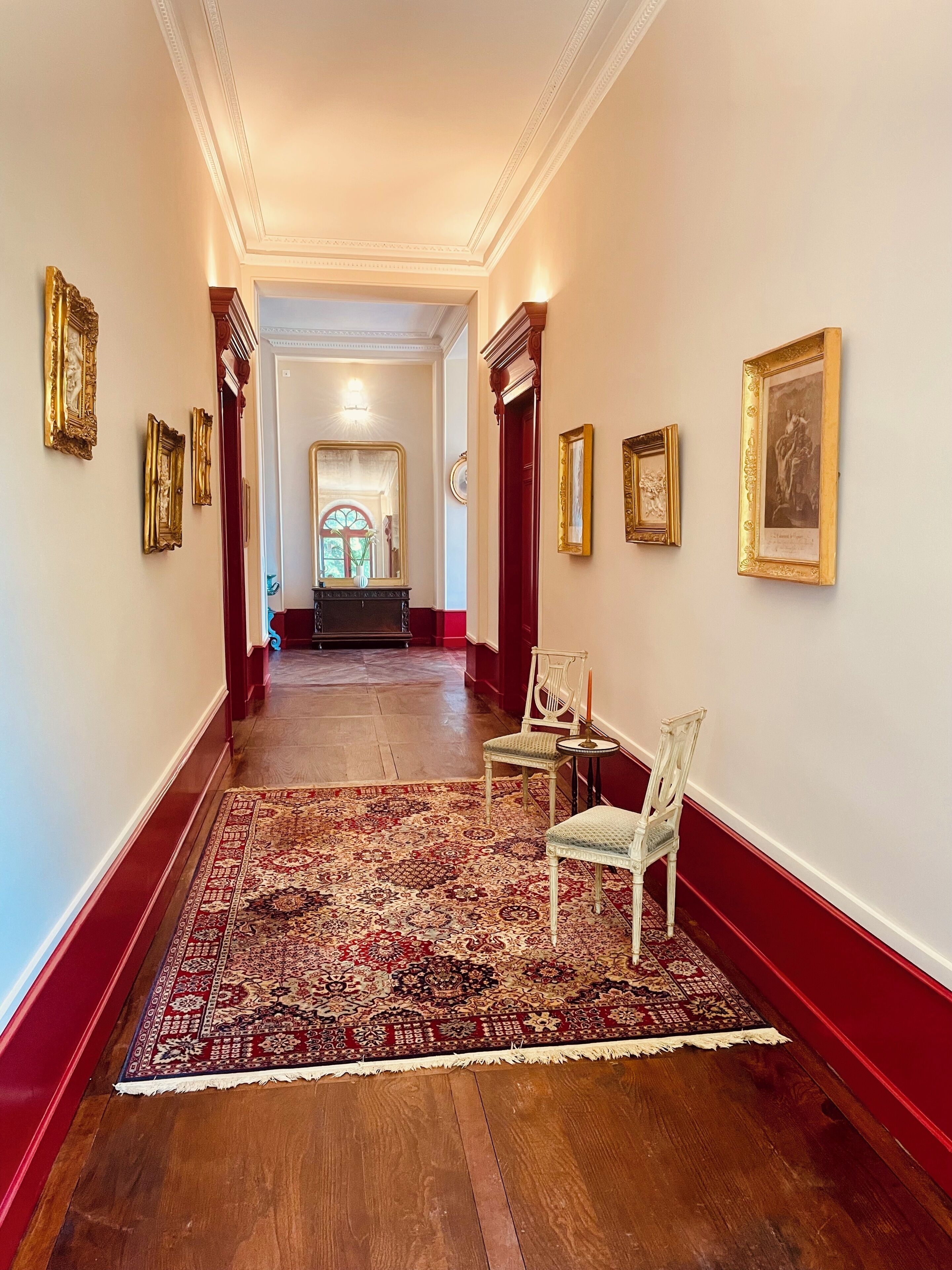 Un couloir avec un tapis à motifs, un plancher en bois et des œuvres d’art encadrées accrochées aux murs.